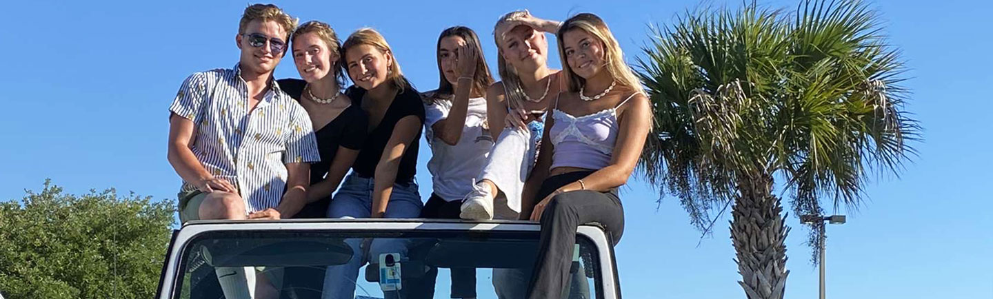students-posing-on-car-1440x434