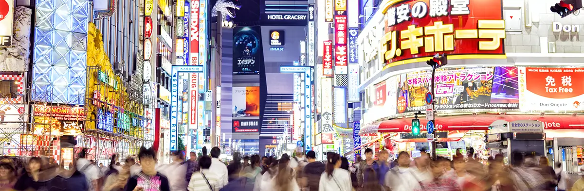 Strade di Tokyo affollate con palazzi illuminate e numerose persone per strada in movimento 